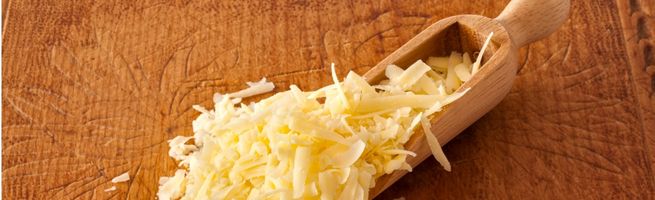 Fromage râpé présenté dans une pelle en bois sur une table rustique, illustrant l'essor des fromages utilisés comme ingrédients en cuisine.