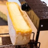 Fromage à raclette en cours de fonte sous un appareil à raclette, illustrant un produit devenu incontournable tout au long de l’année.