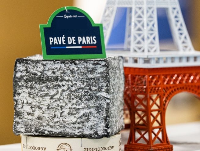 Fromage Pavé de Paris présenté devant une réplique de la Tour Eiffel, mettant en valeur le savoir-faire fromager français et les spécialités régionales.
