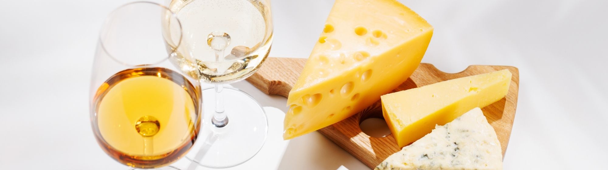 Sélection de fromages affinés présentés sur une planche en bois, accompagnés de deux verres de vin blanc pour illustrer les accords entre fromages et boissons.