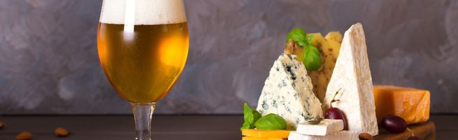 Verre de bière blonde accompagné d’une sélection de fromages affinés disposés sur une table, illustrant l’accord entre bière et fromage.