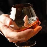 Une main tenant un verre de spiritueux ambré, illustrant la dégustation de boissons alcoolisées et les accords gastronomiques.