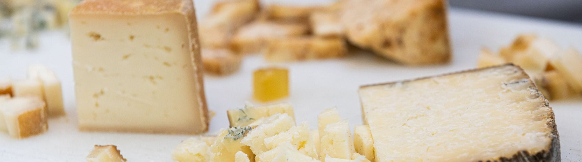 Close-up of an assortment of artisanal cheeses on a wooden board, accompanied by crackers and fruit preserves.