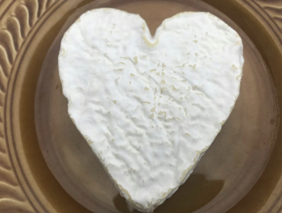 Fromage à croûte blanche en forme de cœur, présenté sur une assiette brune vue de dessus.