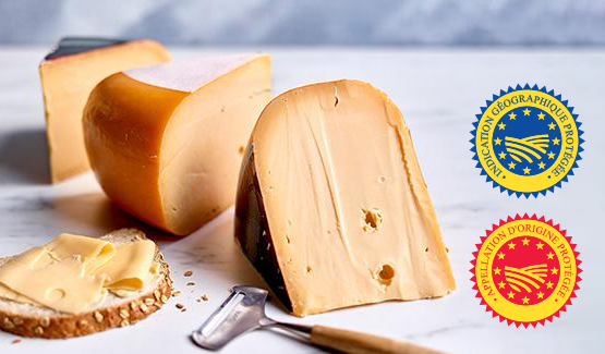 Gros plan sur une meule de fromage à pâte pressée coupée, avec une large tranche dressée, des copeaux de fromage et un couteau au premier plan.