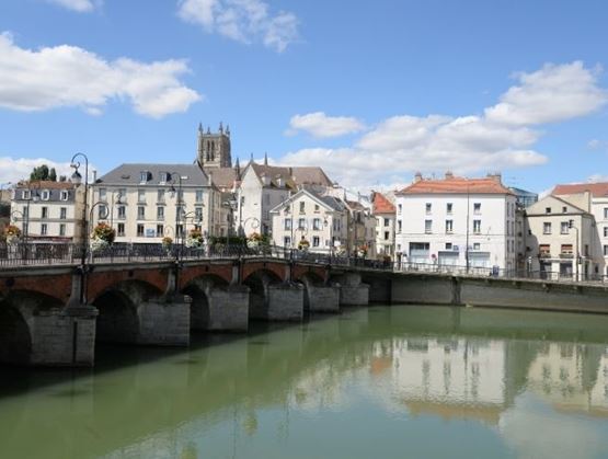 Pont en pierre traversant une rivière dans une ville avec des maisons et une église en arrière-plan.