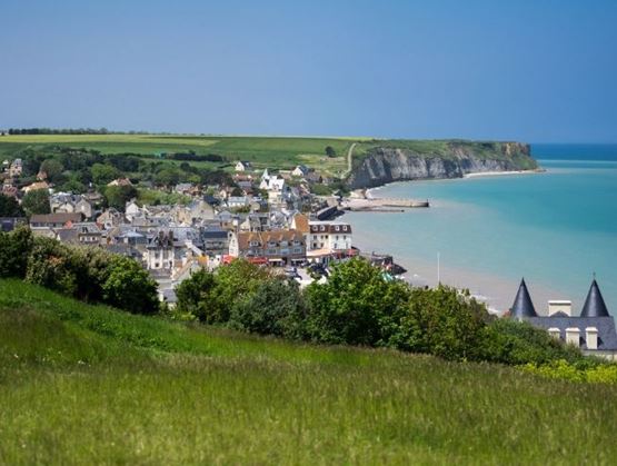 Village côtier avec falaises, maisons et mer turquoise vu depuis une colline.