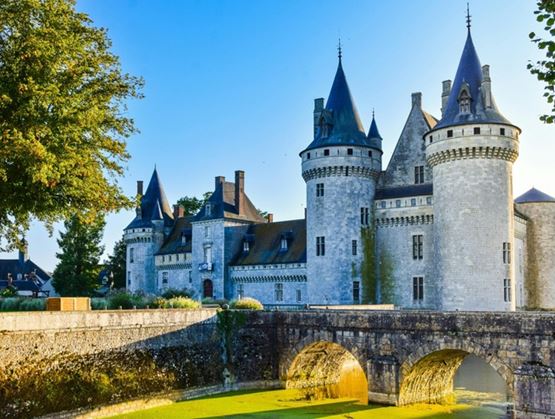 Château en pierre avec tours et pont enjambant des douves dans un cadre verdoyant.
