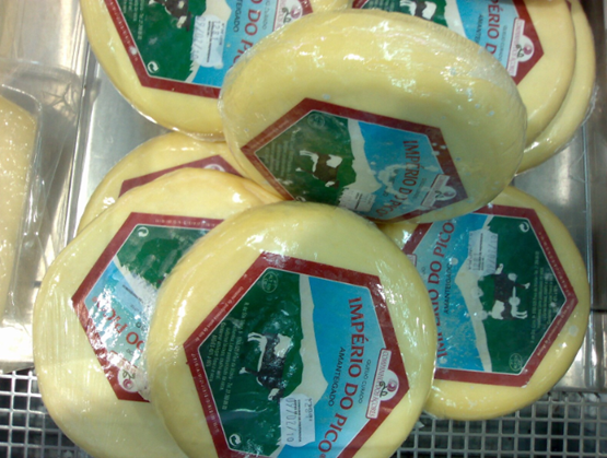 Stacked Portuguese Império do Pico cheeses, with a yellow rind and a green label featuring a cow in front of Mount Pico in the Azores.