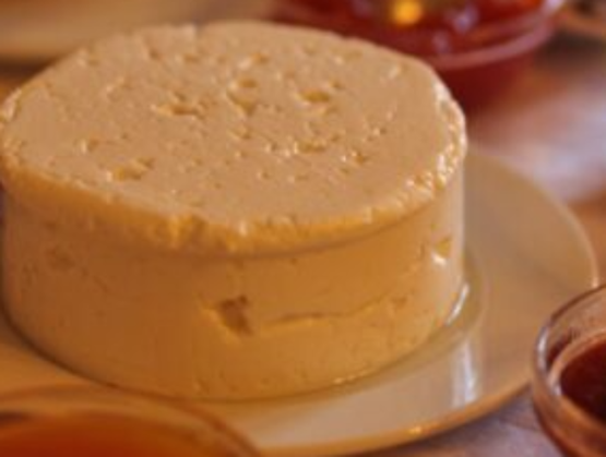 Portuguese fresh Rabaçal cheese presented on a white plate, surrounded by small bowls of jam or condiments.