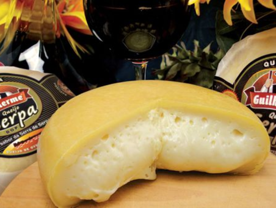 Opened Portuguese Serpa DOP cheese, with a soft texture and yellow rind, presented on a wooden board with a glass of red wine in the background.