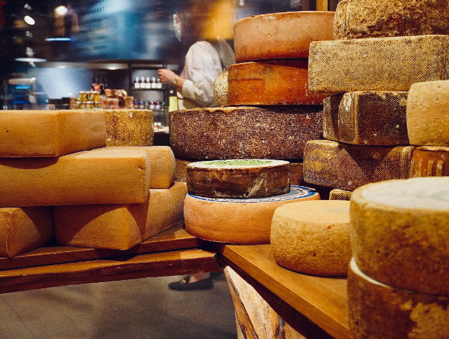 Cheeses of various sizes in the foreground of a cheese shop.