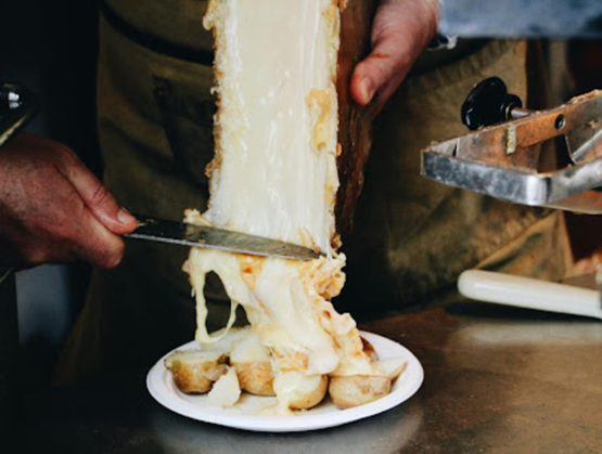 une fondue épaisse allant se posée sur des pommes de terres présentées dans une assiette blanche"