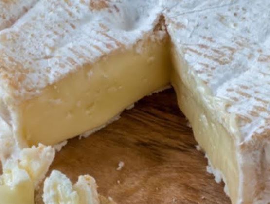 Fromage à pâte molle à croûte blanche, présenté coupé en deux sur une planche en bois, révélant une pâte crémeuse.