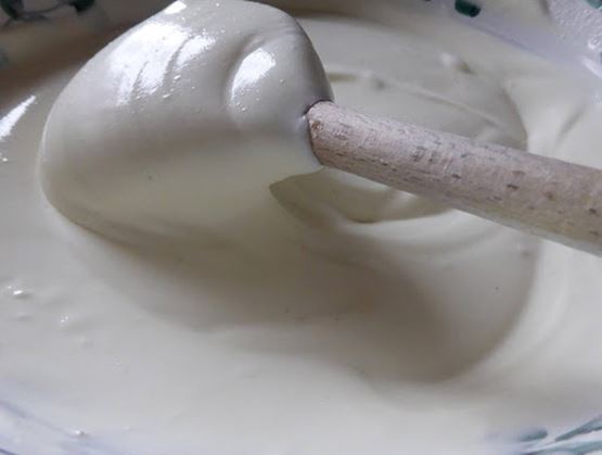 Marshmallow on a stick dipped into a creamy white coating in a bowl, covered with melted white chocolate.