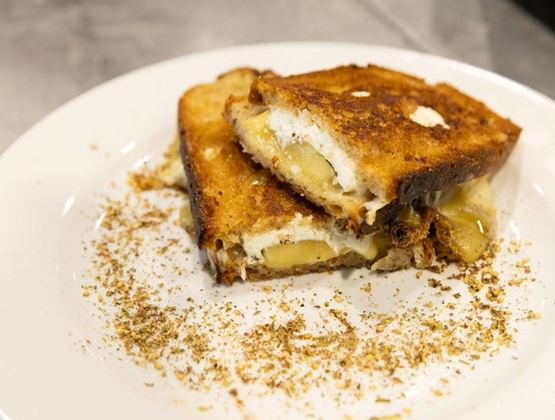 Croque-monsieur grillé au fromage fondu servi dans une assiette avec des épices.