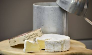 Fromage à pâte molle entamé sur une planche en bois, accompagné de son emballage traditionnel et d’ustensiles en métal en arrière-plan.