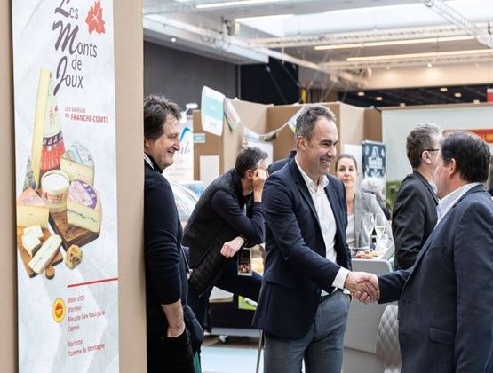 Professionnels échangeant une poignée de main sur un stand de fromages régionaux lors d’un salon.