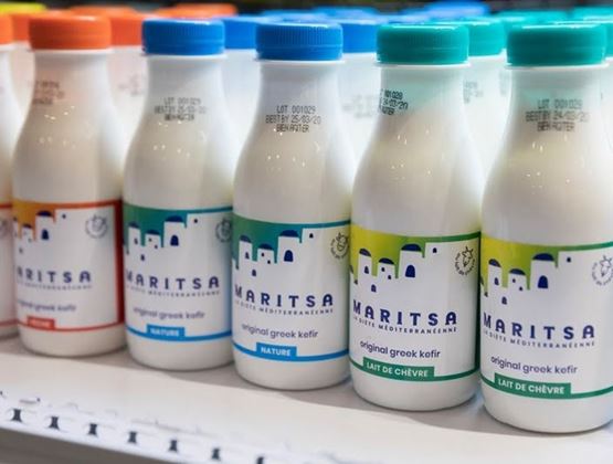 Bouteilles de kéfir grec alignées en rayon réfrigéré lors d’un salon professionnel.