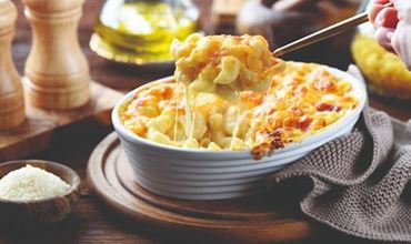 Gratin de pâtes au fromage fondant dans un plat blanc, servi à table avec du parmesan et de l’huile d’olive.