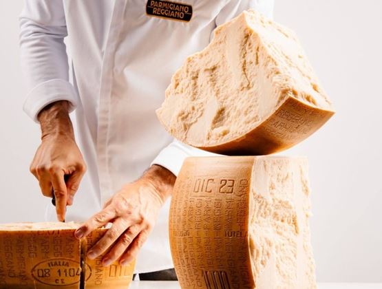 Professionnel découpant une meule de Parmigiano Reggiano sur une table lors d’un salon professionnel.