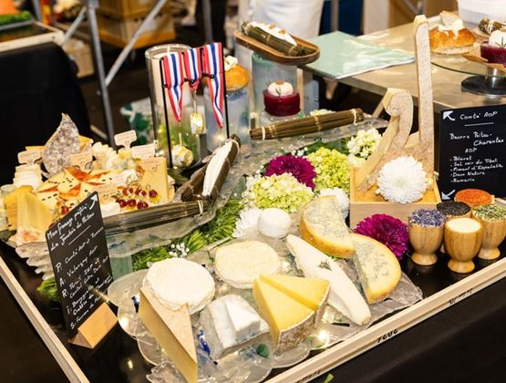 Plateau de fromages présenté lors d’un concours au Salon du fromage et des produits laitiers, décoré de fleurs, d’aromates et de fiches explicatives.