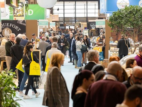Allée fréquentée d’un salon professionnel avec des visiteurs circulant entre plusieurs stands de produits alimentaires.