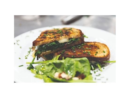 Croque-monsieur grillé garni d’épinards, servi avec une salade verte dans une assiette blanche.
