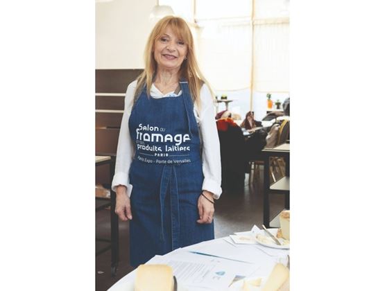 Femme portant un tablier du Salon du fromage et des produits laitiers, debout près d’une table de dégustation.