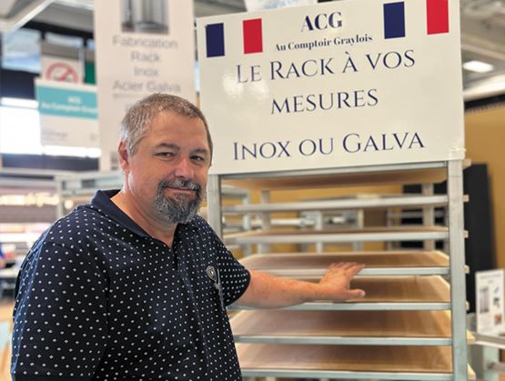 Un homme pose sur un stand professionnel devant un rack sur mesure en inox ou galva.