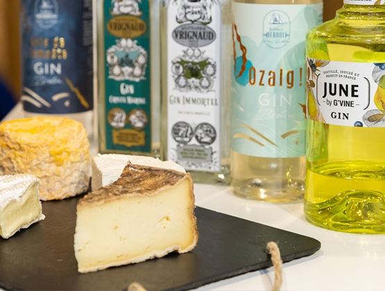 Bouteilles de gin exposées à côté de fromages présentés sur une ardoise lors d’un salon professionnel.