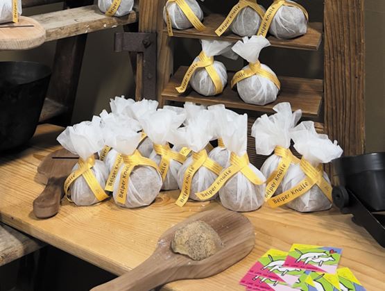 Présentation de fromages emballés dans du papier blanc et fermés par un ruban jaune, disposés sur un stand en bois.