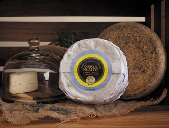 Présentation de fromages affinés sur une étagère en bois, avec une meule emballée, une meule entière et une part sous cloche en verre.