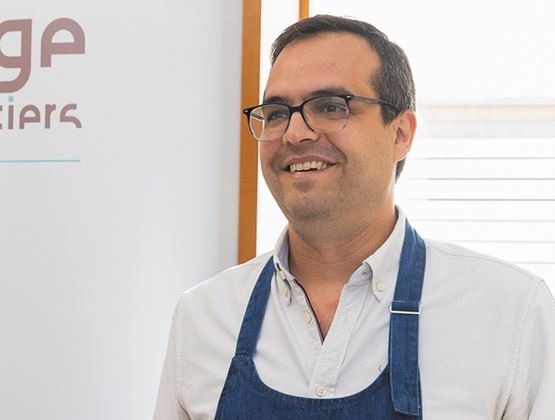 Portrait d’un exposant souriant portant des lunettes et un tablier bleu lors d’un salon professionnel.
