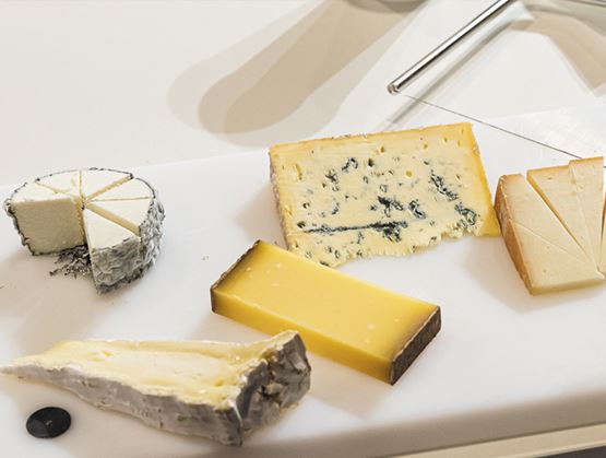 Assortiment de fromages découpés sur un plateau blanc, avec des parts de fromage bleu, de chèvre, de tomme et de fromage à pâte pressée.