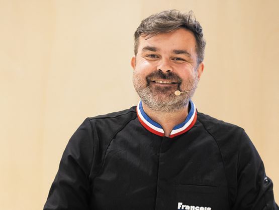 Portrait d’un homme souriant en tenue professionnelle noire avec col tricolore et micro-casque.