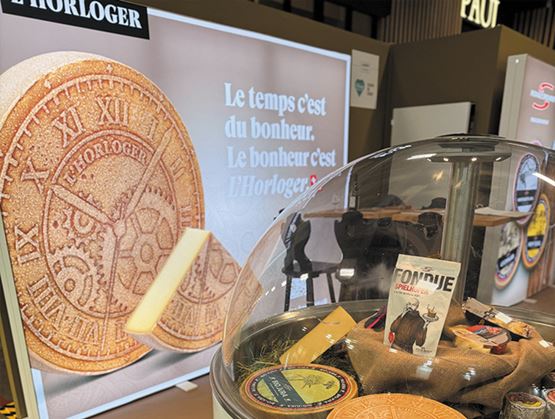 Stand de fromages présentant L’Horloger, avec une vitrine de produits et un visuel promotionnel mettant en avant une meule de fromage.