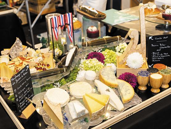 Présentation raffinée de différents fromages sur un stand, avec des fleurs, des ardoises descriptives et des décors autour des produits.