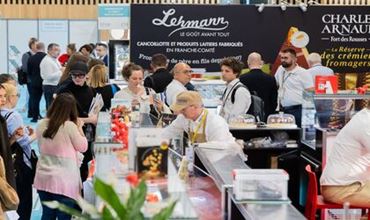 Stand alimentaire animé lors d’un salon professionnel, avec visiteurs, exposants et produits présentés en dégustation.