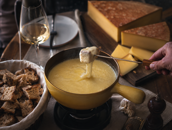 Fondue au fromage servie dans un caquelon, accompagnée de pain, de vin blanc et de meules de fromage.