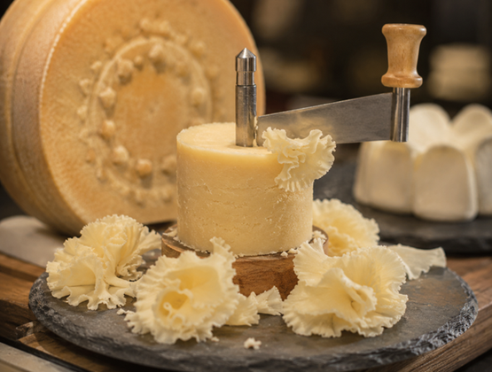 Fromage raclé à la girolle en fines rosettes, présenté avec une meule en arrière-plan.