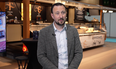 Homme interviewé devant le stand de la Fromagerie Crèmerie au sein d’un salon professionnel.