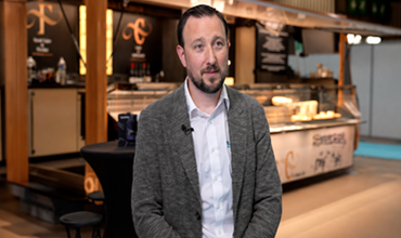 Homme interviewé devant le stand de la Fromagerie Crèmerie au sein d’un salon professionnel.