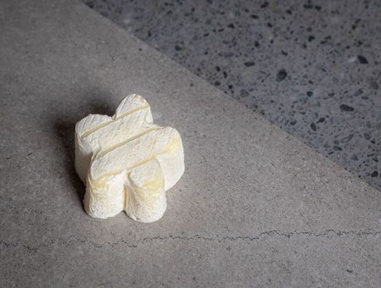 Petit fromage blanc moulé en forme de fleur, posé sur une surface minérale grise.