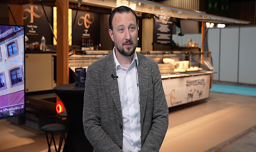 Homme interviewé devant le stand de la Fromagerie Crèmerie au sein d’un salon professionnel.