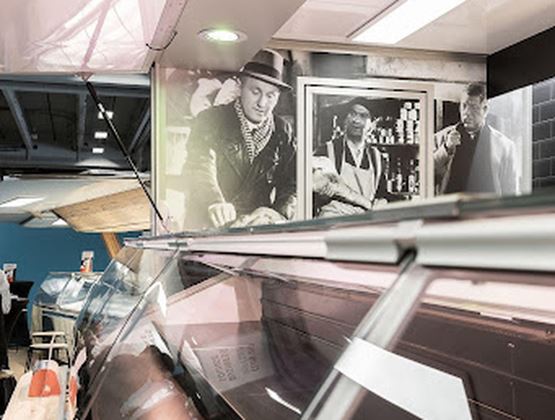 Vitrine réfrigérée d’une fromagerie, devant un mur décoré de photographies anciennes en noir et blanc.
