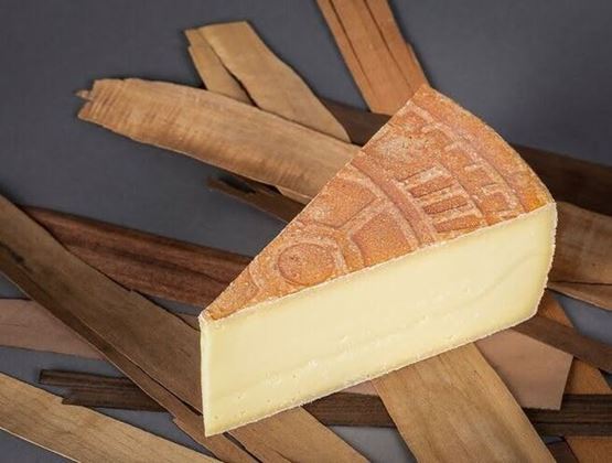 Part de fromage à pâte pressée avec croûte gravée, présentée sur des lanières de bois.