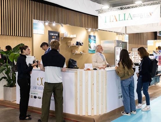 Stand collectif italien sur un salon professionnel, avec exposants et visiteurs en discussion.