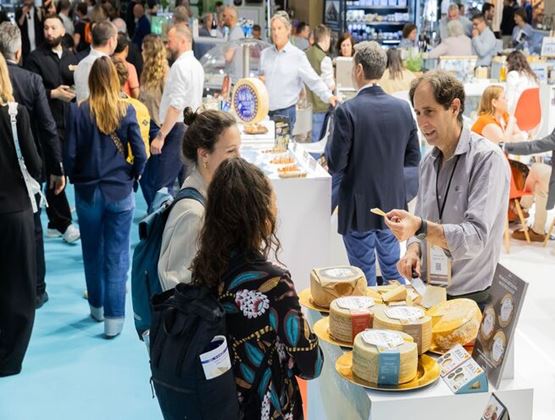Visiteurs échangeant avec un exposant autour de fromages présentés sur un stand lors d’un salon professionnel.