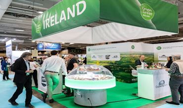 Pavillon de l’Irlande sur un salon professionnel, avec visiteurs et produits alimentaires exposés.